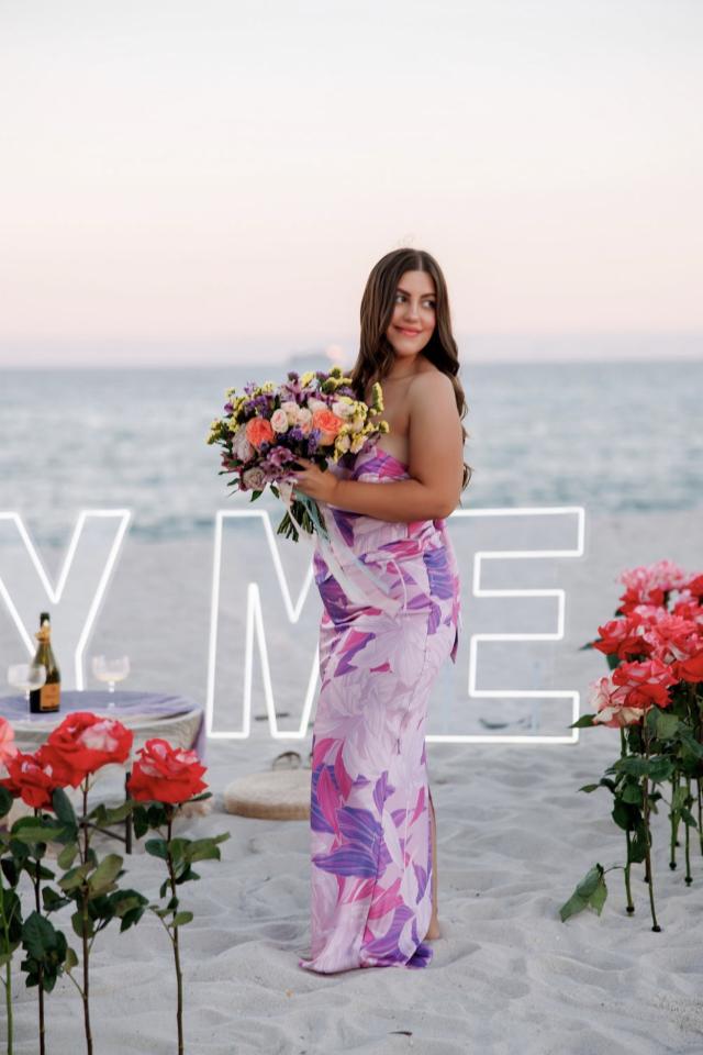 Woman holding a bouquet beside colorful Miami Beach proposal décor