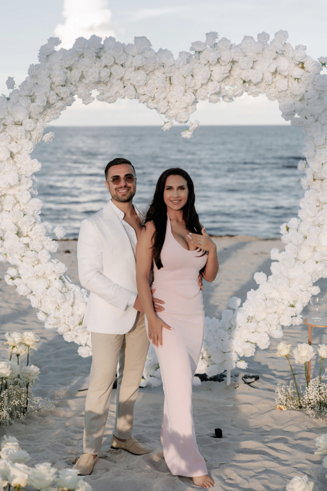 Couple posing inside a white heart-shaped rose arch on Miami Beach