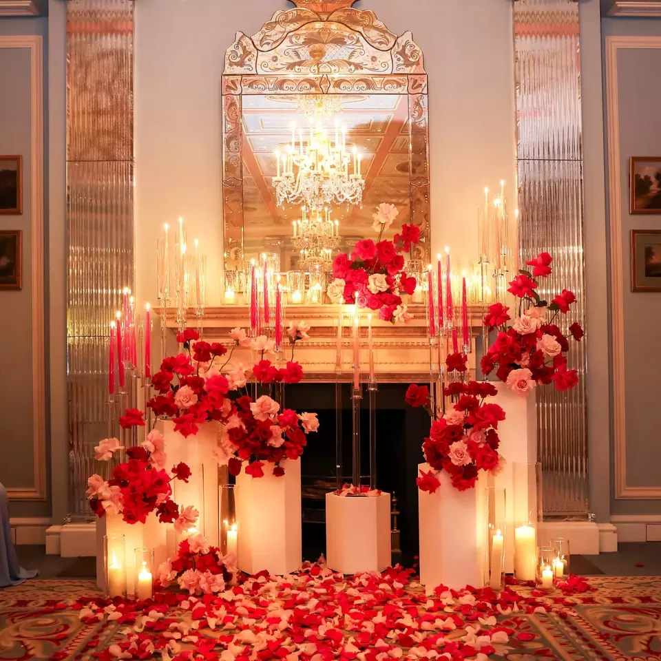 A candlelit proposal setup in a chandeliered room at The Lanesborough, with tall red tapers, roses and petals across the floor.