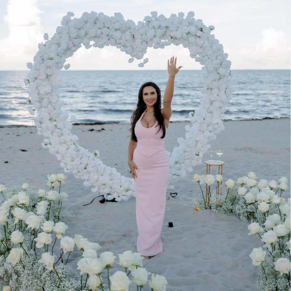Woman posing beside a white floral heart arch on Miami Beach